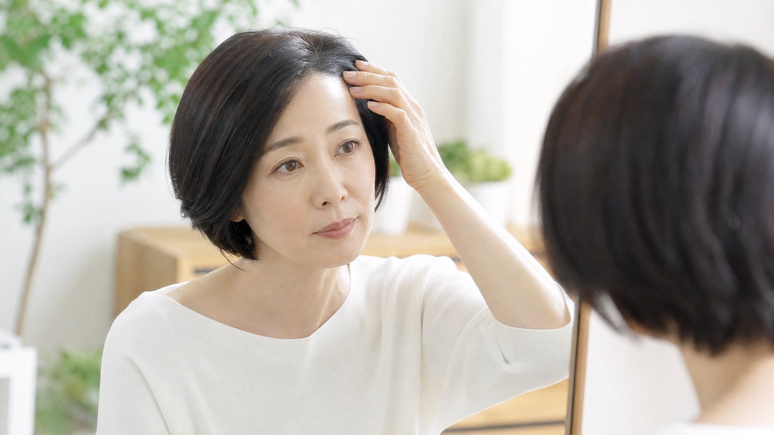 明るい室内で頭皮に指をあてる女性。頭が痒いのが気になる場面のイメージ写真。